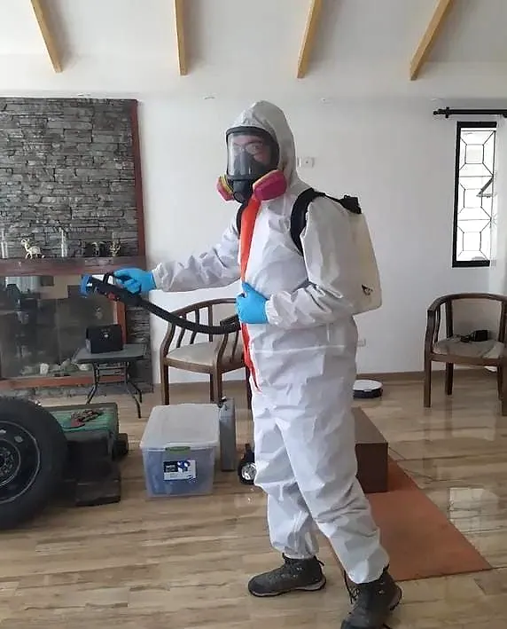 Técnico con traje blanco y máscara aplicando tratamiento en el interior de una vivienda
